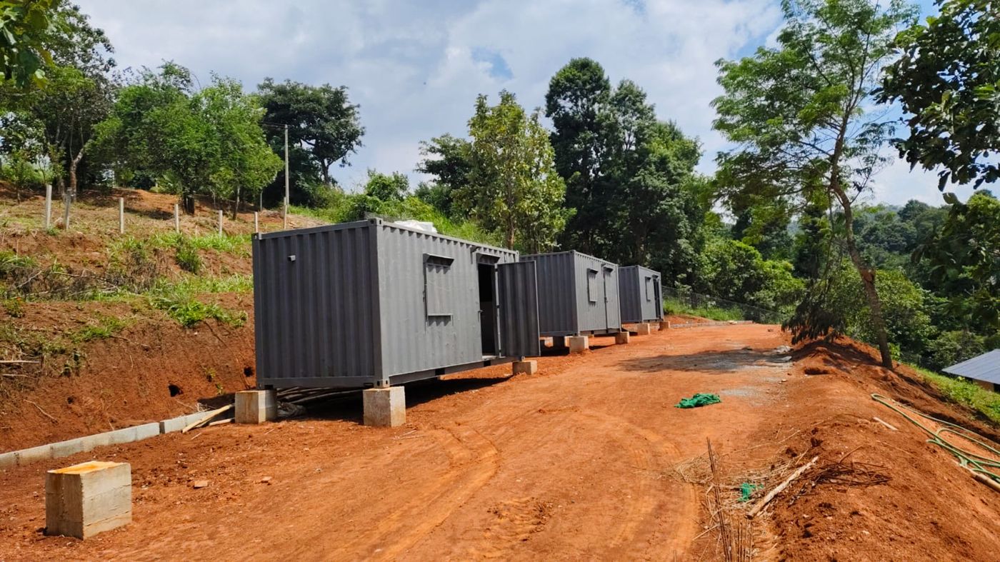 Three grey steel containers set on concrete plinths along a red earth track